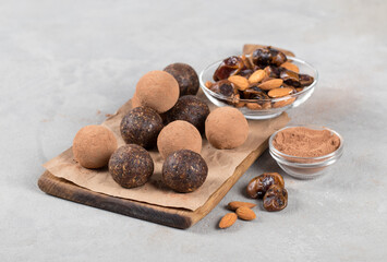 Vegan truffles made of dates, almonds and cocoa on a wooden board on a light gray background