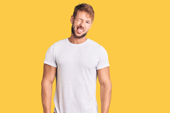 Young caucasian man wearing casual white tshirt winking looking at the camera with sexy expression, cheerful and happy face.
