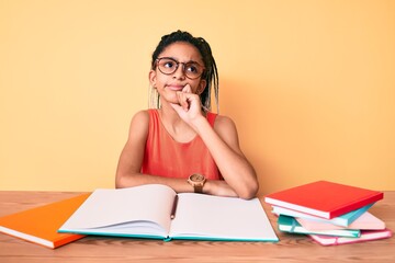 Young african american girl child with braids studying for school exam serious face thinking about...