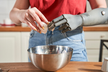 Woman chef with artificial limb breaking eggs into a plate