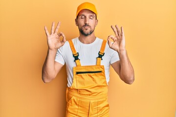 Young handsome man wearing handyman uniform over yellow background relaxed and smiling with eyes closed doing meditation gesture with fingers. yoga concept.