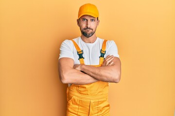 Young handsome man wearing handyman uniform over yellow background skeptic and nervous, disapproving expression on face with crossed arms. negative person.