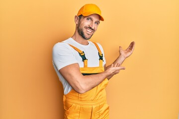 Young handsome man wearing handyman uniform over yellow background inviting to enter smiling...