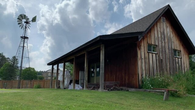 A traditional homestead farmhouse is seen with a windmill spinning in the wind providing power for a water pump. 