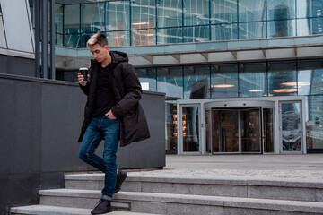 A young man walking down the street and drinking coffee. Everyday life in a big city. Coffee and books. Street in the winter.