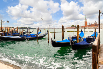Naklejka premium Gondolas dock along the Grand Canal with the Riva di Schiavoni and the Church and island of San Giorgio Maggiore visible in the distance in Venice, Italy.