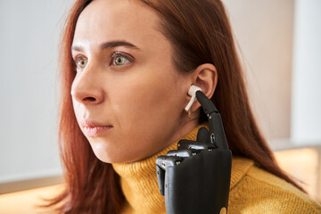 Woman with prosthesis arm listening music in headphones
