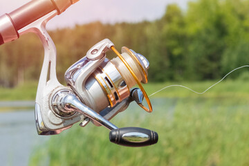 old spinig reel on the background of the lake and forest. spinning detail, close up