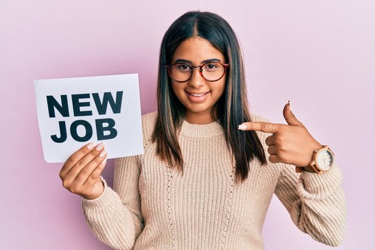 Young latin girl holding new job message on paper smiling happy pointing with hand and finger