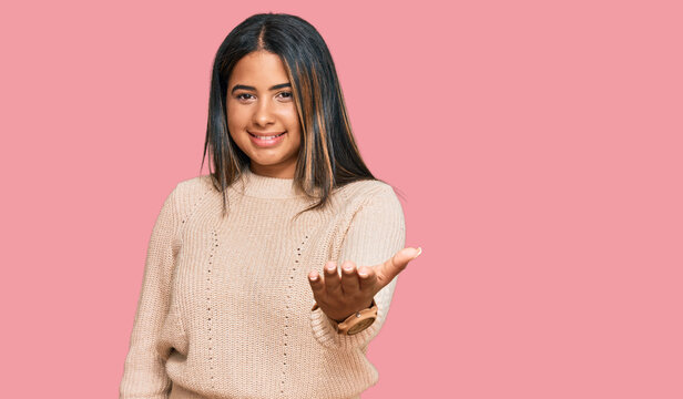 Young latin girl wearing wool winter sweater smiling cheerful offering palm hand giving assistance and acceptance.