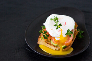 Delicious poached egg sandwich, smoked salmon and avacado on a black plate.