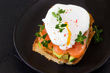 Delicious poached egg sandwich, smoked salmon and avacado on a black plate.