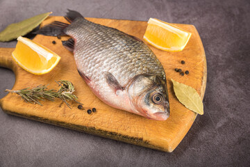 Fish Carp not peeled on a cutting board with lemon and spices on a gray mottled background