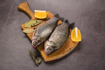 Fish Carp not peeled on a cutting board with lemon and spices on a gray mottled background