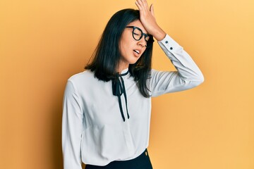 Beautiful asian young woman wearing business shirt surprised with hand on head for mistake,...