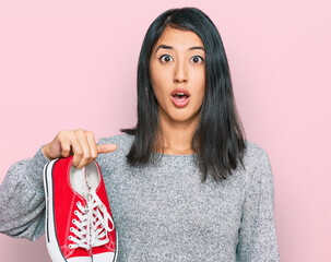 Beautiful asian young woman holding red casual shoes scared and amazed with open mouth for surprise, disbelief face