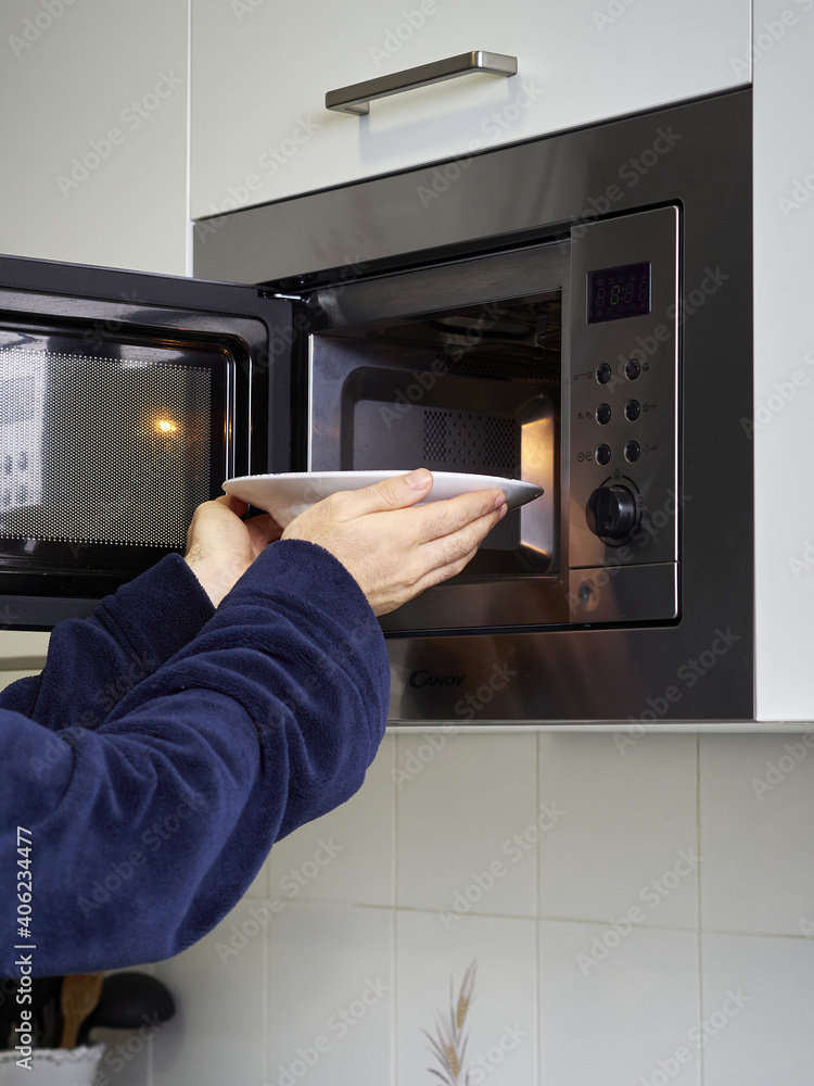 Wall mural vertical shot of a male putting a plate in the microwave