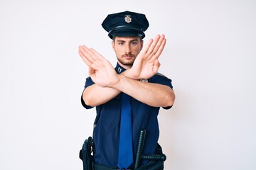 Young caucasian man wearing police uniform rejection expression crossing arms and palms doing negative sign, angry face