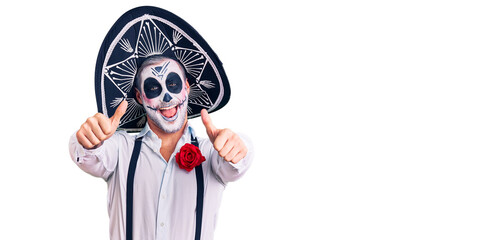 Man wearing day of the dead costume over background approving doing positive gesture with hand, thumbs up smiling and happy for success. winner gesture.
