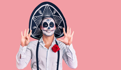 Man wearing day of the dead costume over background showing and pointing up with fingers number nine while smiling confident and happy.