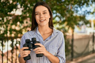 Young hispanic girl smiling happy using binoculars at the park.