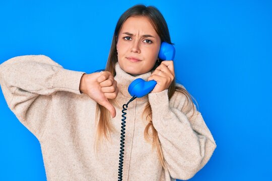 Beautiful caucasian woman speaking on vintage telephone with angry face, negative sign showing dislike with thumbs down, rejection concept