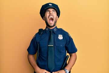 Handsome hispanic man wearing police uniform angry and mad screaming frustrated and furious,...