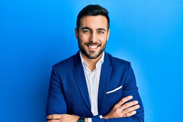Young hispanic businessman wearing business jacket happy face smiling with crossed arms looking at...