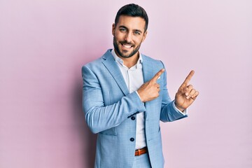 Young hispanic businessman wearing business jacket smiling and looking at the camera pointing with two hands and fingers to the side.