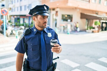 Young hispanic policeman wearing police uniform with serious expression. Drinking cup of take away...