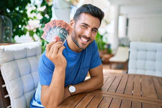Young hispanic man smiling happy holding australian dollars banknotes at the terrace.