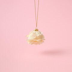 Cream rose hanging like a Christmas ball against pink background. Creative New Year concept.