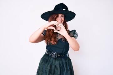Young beautiful woman wearing witch halloween costume smiling in love doing heart symbol shape with hands. romantic concept.