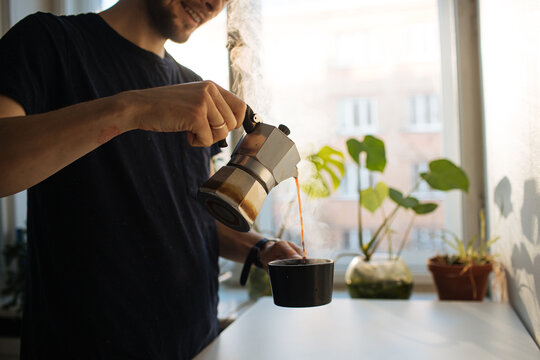 Man making morning coffee in moka espresso pot. Flavorful coffee at home kitchen. Male pouring coffee in a cup. Guy morning cozy ritual. Breakfast lighter roast blend. Home leisure fika at holidays	
