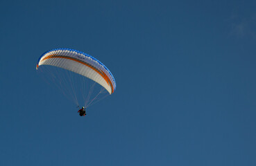 A beautiful view of a paraglide flying gliding on a clear blue sky at the golden hour with a nice wind windy breeze on a sunny day 