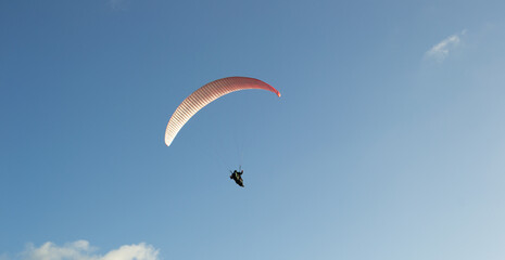A beautiful view of a paraglide flying gliding on a clear blue sky at the golden hour with a nice wind windy breeze on a sunny day 