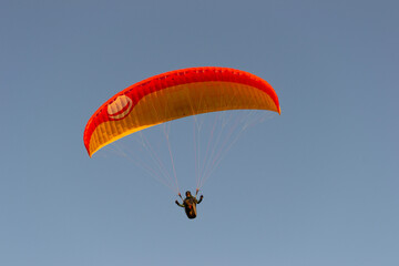 A beautiful view of a paraglide flying gliding on a clear blue sky at the golden hour with a nice wind windy breeze on a sunny day 
