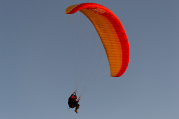 A beautiful view of a paraglide flying gliding on a clear blue sky at the golden hour with a nice wind windy breeze on a sunny day 