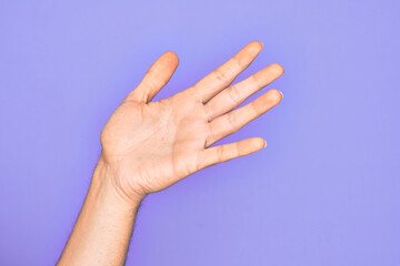 Hand of caucasian young man showing fingers over isolated purple background presenting with open palm, reaching for support and help, assistance gesture