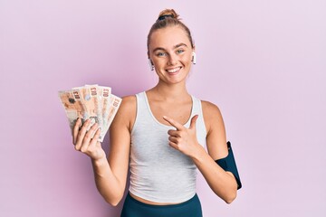 Beautiful blonde sport woman holding 10 united kingdom pounds banknotes smiling happy pointing with hand and finger