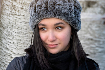 Closeup winter portrait of a beautiful young woman in a gray hat and black coat gazing off to the side