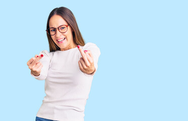 Beautiful brunette young woman wearing casual white sweater and glasses showing middle finger doing...