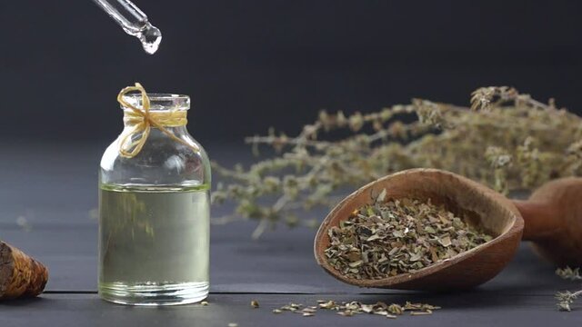 Glass bottle of thyme essential oil and bunch of dry thyme on black wooden rustic background, oil dripping