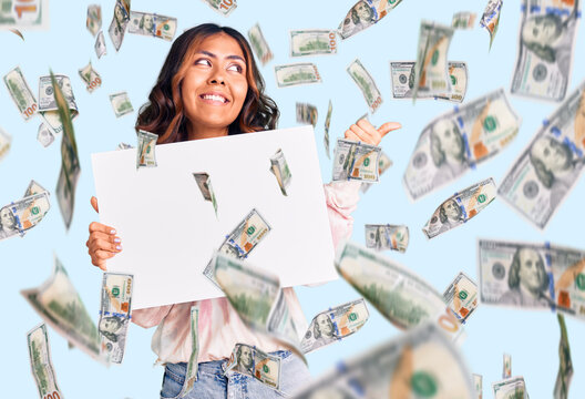 Young beautiful mixed race woman holding cardboard banner with blank space pointing thumb up to the side smiling happy with open mouth