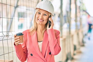 Young caucasian architect woman talking on the smartphone and drinking coffee at the city