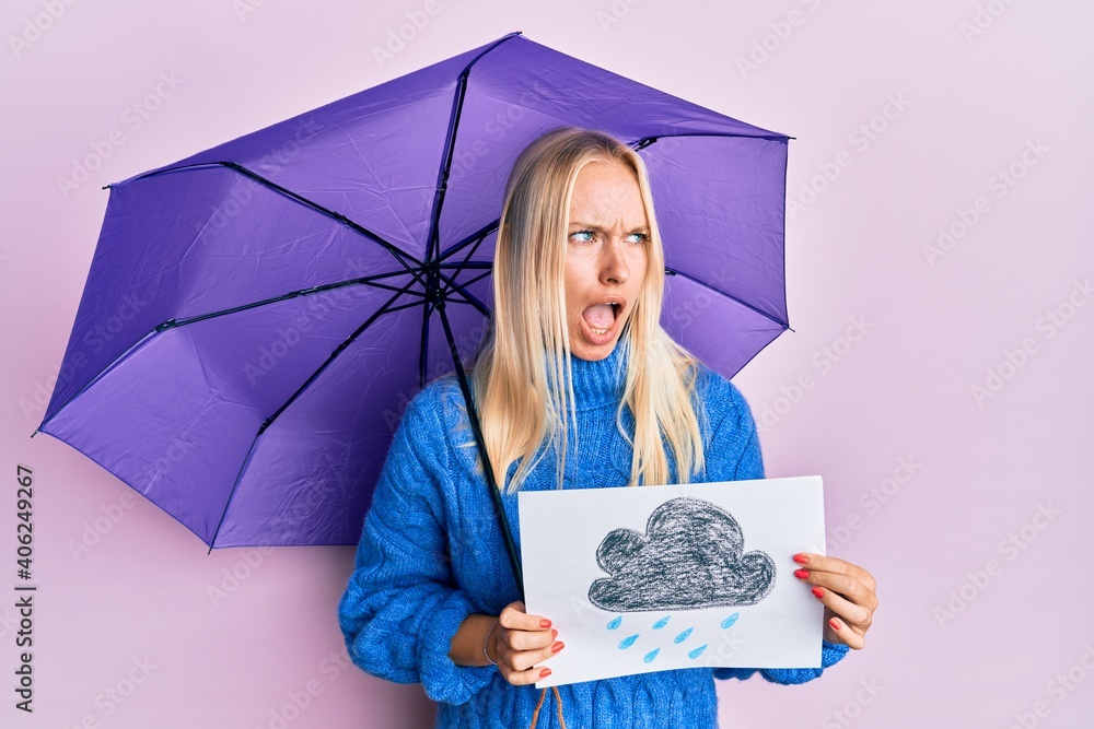 Poster Young blonde girl holding umbrella rain draw angry and mad screaming frustrated and furious, shouting with anger. rage and aggressive concept.