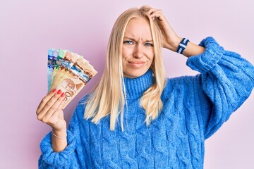 Young blonde girl holding canadian dollars confuse and wondering about question. uncertain with...