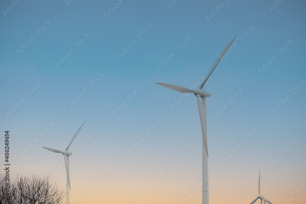 Wall mural 2 white wind turbines with blue and yellow sky in the background