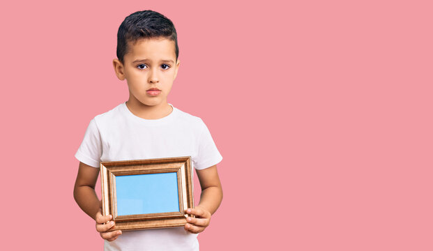 Little cute boy kid holding empty frame thinking attitude and sober expression looking self confident
