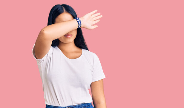 Young beautiful asian girl wearing casual clothes and glasses covering eyes with arm, looking serious and sad. sightless, hiding and rejection concept